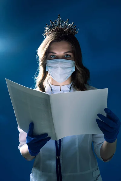 Salgının yayılmasını önleme ve koronavirüs COVID-19 'u tedavi etme kavramı. Korku filmi gibi, maskeli bir doktorun portresi ve karanlık mistik atmosferde bilgi dergisi tutan eldivenler. 