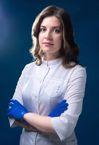 Mavi arka planda resmi duruş içinde eldivenli pozitif bir doktorun portresi.