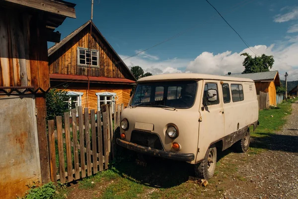 Sovyet 4WD minibüsü Rus köyündeki ahşap evin yanında duruyor.