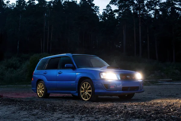 Mavi spor jdm araba Subaru Forester STi far açık kumsalda ve arka planda karanlık orman
