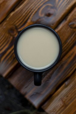 Sütlü, siyah kahve fincanı ıslak, ahşap kahverengi masada.