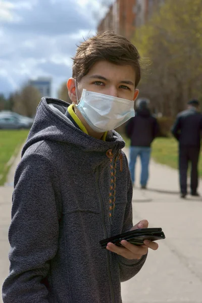 teen in a medical mask on the street with a phone