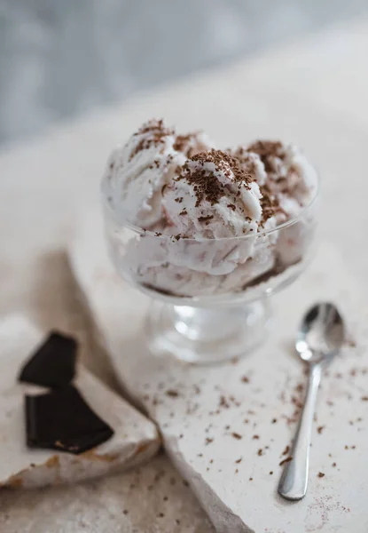 Gelato alla vaniglia cosparso di gocce di cioccolato in una ciotola trasparente su uno sfondo di pietra chiara — Foto Stock