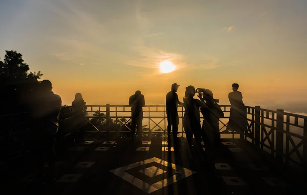 silhouette image of group of people on sunrise time at high view point with sun in background.