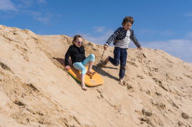 Çocuklar bir tahtanın üzerindeki kumdan kayıyor.