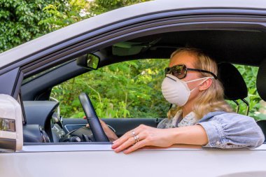Koronavirüs salgını sırasında koruyucu maskeli bir kadın araba kullanıyor.