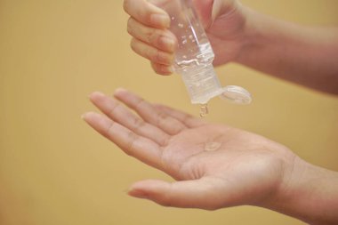 Turuncu arka planı olan el dezenfektanı kullanarak elini kapat..