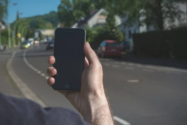 Mann hält und sieht sein iPhone mit einer Straße im Hintergrund — Stockfoto