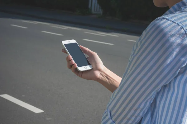 Жінка йде по міській вулиці зі своїм білим iPhone на сонці — стокове фото