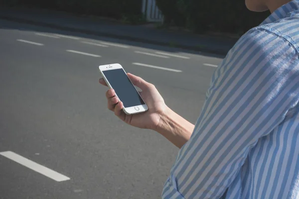 Mujer está caminando por la calle de la ciudad con su iPhone blanco al sol —  Fotos de Stock