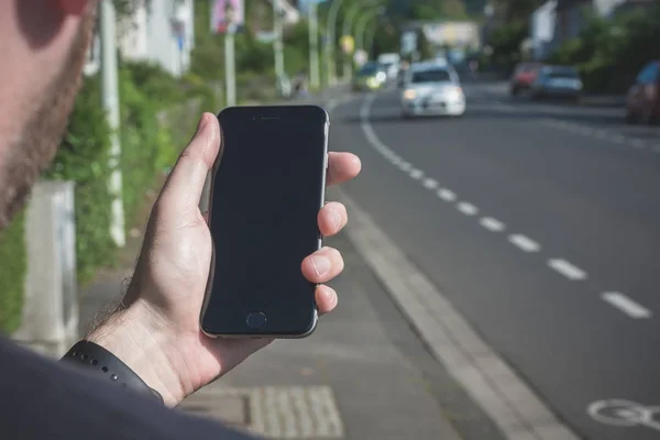 Joven mira su iPhone negro en la ciudad — Foto de Stock