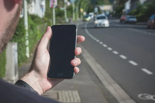 A fiatalember a város úgy néz ki a fekete iphone — Stock Fotó