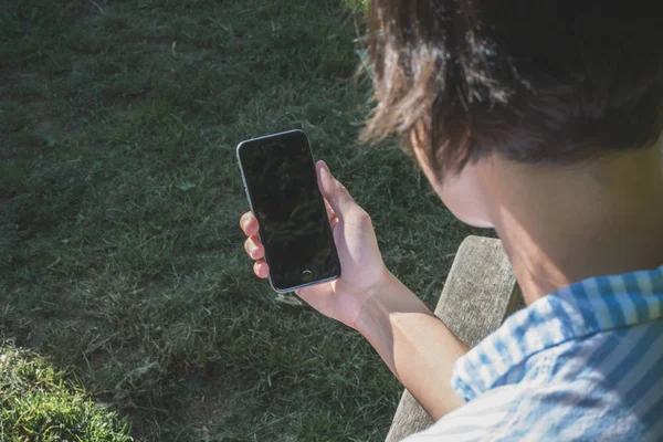 Mulher está sentada em um banco e olhando seu smartphone — Fotografia de Stock