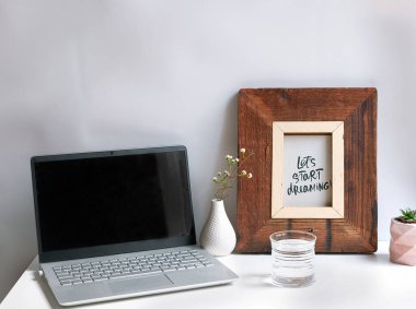Beyaz arka planda bir defter, bir bardak su, bir vazo çiçek ve bir poster. Evden çalışıyorum. İş yeri. Basitlik ve minimalizm kavramı. Karantinaya alınmış yaşam.