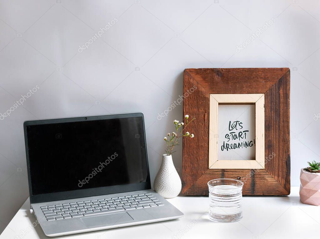 Notebook on a white background, a glass of water, a vase of flowers and a poster. Work from home. Workplace. The concept of simplicity and minimalism. Quarantined life.