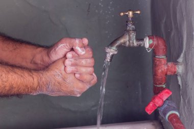 Zavallı bir tuvalette ellerini tarafsız sabun ve suyla yıkayan bir adam.