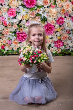 Mutlu küçük kız elinde çiçeklerle dolu bir sepet tutan beyaz bir elbise giyiyor. Çiçeklerle dolu bir arka planda oturuyor. Anneme bir hediye.