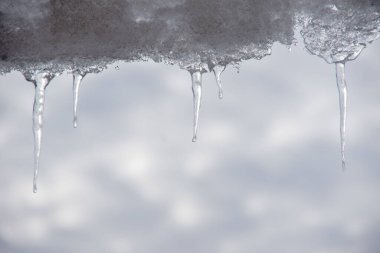 Açılış, güneşin mavi bir gökyüzüne karşı buz saçağı ile evin çatısından sarkan buz saçakları ile bahar manzarası..