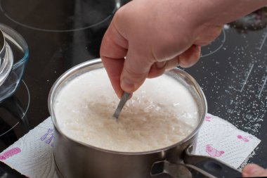 Bir elin yakınlaşması, arka plandaki metal kasede kaynamış pirinci ters çevirir. Sağlıklı kahvaltı kavramı. Kahvaltı gevreği menüsü, üst görünüm..