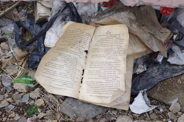 Crumpled dirty torn book lies on the ground among various rubbish.