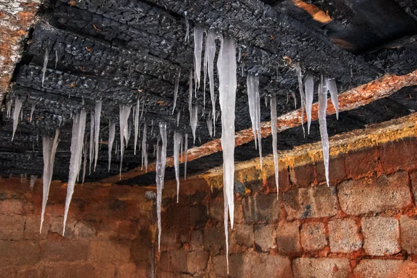 Close-up of an old house with a charred ceiling from which white icicles hang