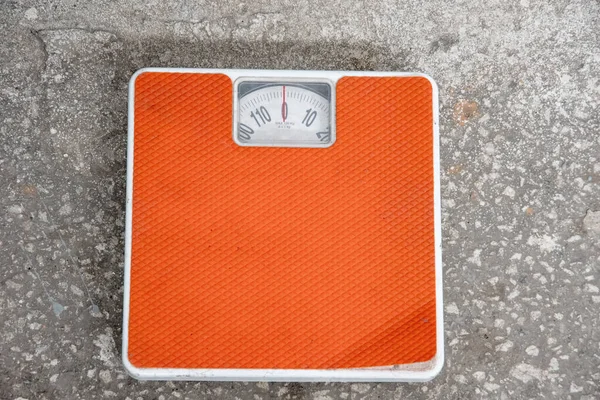 Top view of an old orange mechanical scale standing on a stone floor. Scales used a lot. The concept of losing weight, healthy living