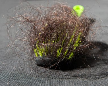 Siyah ve yeşil tarağın üzerinde uzanan kıvrımlı kahverengi insan saçı yığını, seçici odaklanma. Kırılgan kılsız kellik.