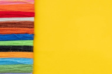 Nakış işlemek için çok renkli iplik sarı arka planda bir sıraya dizilir. Üst görünüm, kopyalama alanı, düz uzanma.