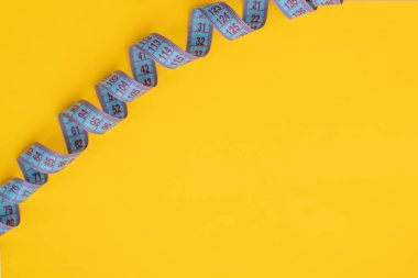 Sarı arka plandaki tasarımın için mavi bir terzi ölçüm bandının yakın çekimi. Ağırlık ve ses kontrolü için santimetre bant. Düz yat, boşluğu kopyala