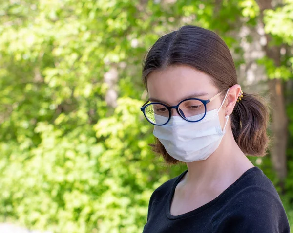 Retrato de cerca de una hermosa joven con una máscara médica desechable en el parque. Copiar espacio — Foto de Stock