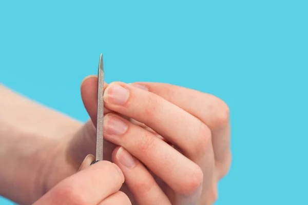 A mulher poliu pregos com um arquivo de prego em um fundo azul, close-up, espaço de cópia. A ideia de auto-cuidado de unhas, mãos — Fotografia de Stock