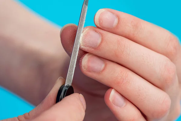 Mãos de uma mulher caucasiana a polir as unhas com uma lima de prego num fundo azul, close-up. A ideia de auto-cuidado de unhas, mãos — Fotografia de Stock