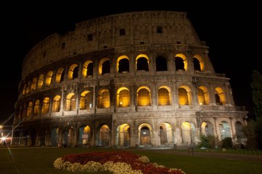 Turistsiz Colosseum manzarası. Gece manzarası. Ön planda kırmızı ve beyaz çiçekler. Roma 'nın en popüler turistik merkezi.. 