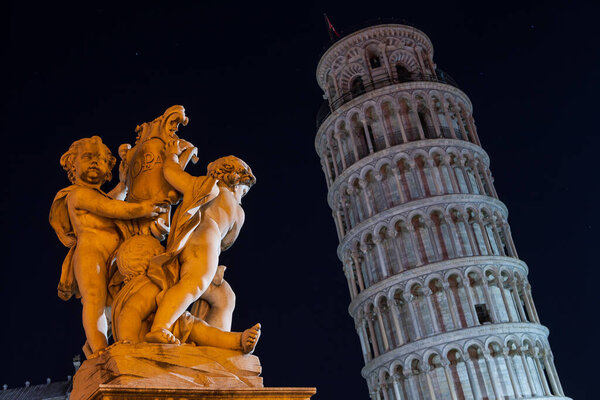 The Leaning  Tower of Pisa  in the background and angels statue in the foreground. Night landscape. Cathedral Square.Campo Dei Miracoli, Europe, Italy, Pisa, Tuscany.   The most popular tourist attractions in Tuscany. 