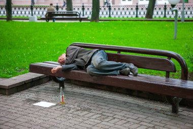 Minsk, Mikhailovsky Meydanı, Belarus, 12.05.2010. Evsiz bir adam yazın şehirdeki parktaki ahşap bankta uyur. Bankın yanındaki tohumlardan çıkan açık şarap ve kabuk şişesi. Sosyal belgesel konsepti, seçici odak. 