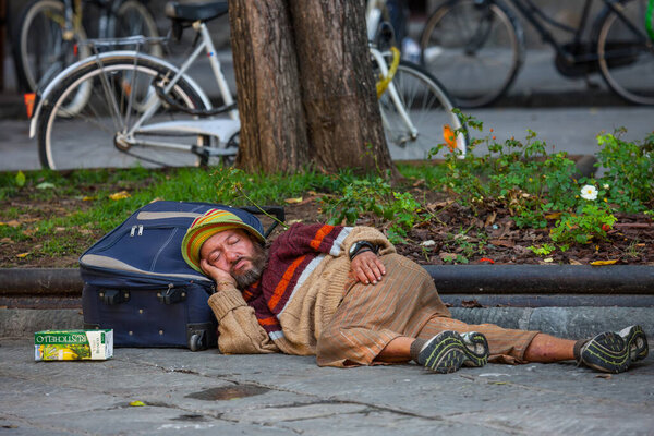 Флоренция (Chisea di San Spirito), Италия, 02.10.2012. Бездомный грязный мужчина в зеленой шляпе и бежевом свитере спит на чемодане. Концепция социальной документации, избирательная направленность. Мнение Феттеля
.