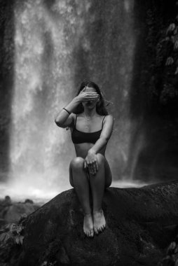 Bali 'de bir ormanda şelalede bikinili bir kız poz veriyor.