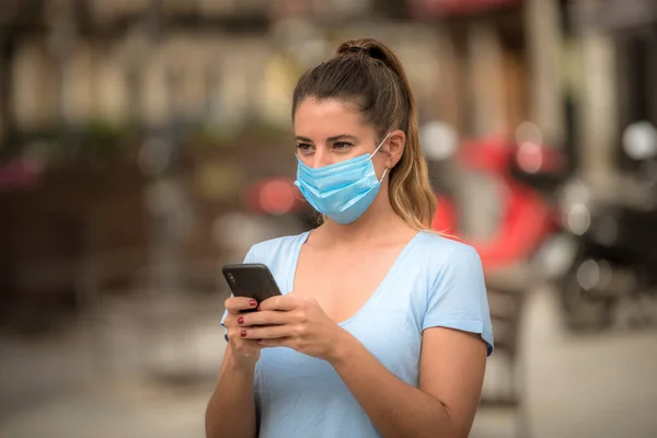 girl uses a phone in the street with a medical mask during the coronavirus quarantine