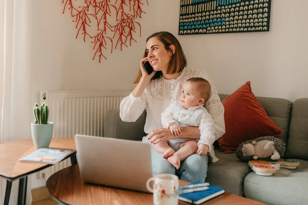 young business mother is using a laptop and smiling while spending time with her cute baby at home