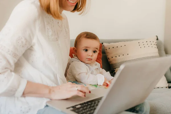 young business mother works from home with her laptop, with her baby by her side having fun