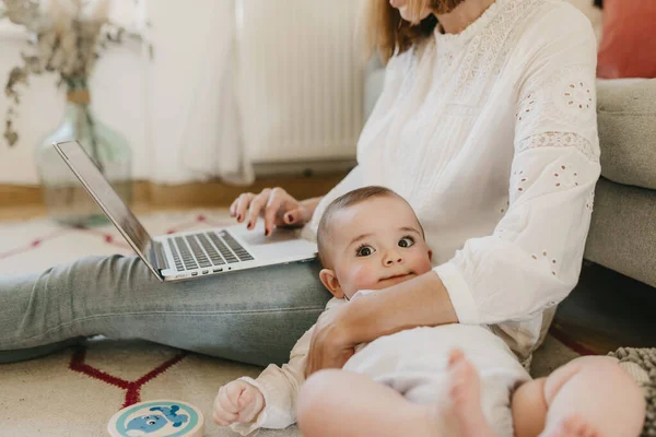 young business mother works from home with her laptop, with her baby by her side having fun