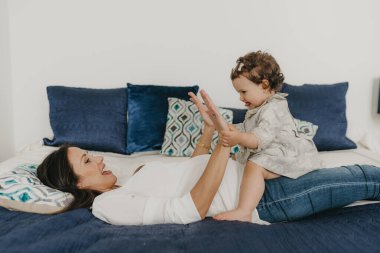 Genç ve güzel anne kızıyla evde yatakta oynuyor.