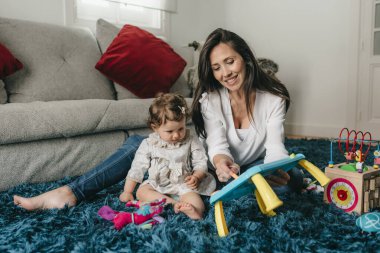 Genç ve güzel anne, kızıyla evdeki oturma odasında yerde oynuyor.