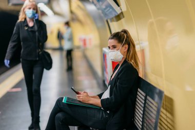 Genç bayan elinde tıbbi bir maskeyle metroyu bekliyor.