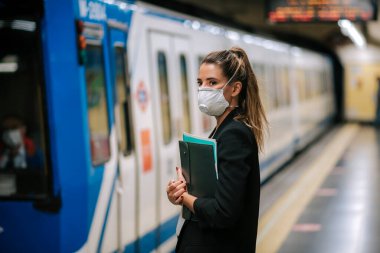 Genç bayan elinde tıbbi bir maskeyle metroyu bekliyor.