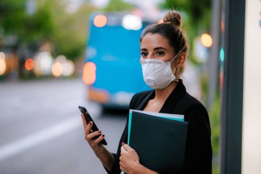 Sağlık maskeli genç iş kadını otobüsü bekliyor.