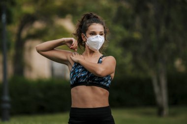 Tıbbi maske takan bir kaçakçı, Coronavirüs salgını Covid-19. Spor, karantinada aktif yaşam yüz maskesi korumalı cerrahi sterilizasyon. Corona Salgını 'nda atletizm pistinde açık hava koşusu. yoga parkı