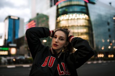Güzel İspanyol kadın kulaklıkla müzik dinliyor ve dışarıda akıllı telefonlar çalıyor. Spor elbiseli, kıvırcık saçlı, şehirli bir Latin kız. Gece şehri