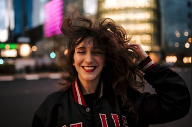 Güzel İspanyol kadın kulaklıkla müzik dinliyor ve dışarıda akıllı telefonlar çalıyor. Spor elbiseli, kıvırcık saçlı, şehirli bir Latin kız. Gece şehri