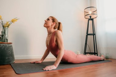 Güzel sarışın kadın evde antrenman yapıyor. Kadın evde yoga yapıyor. Sağlıklı ve aktif yaşam tarzı için egzersiz dersleri alan formda bir kız. Kadın evde çalışmak için karantina kullanıyor. Evimde geriniyorum